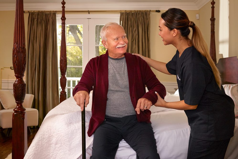 Caregiver helping senior man out of bed