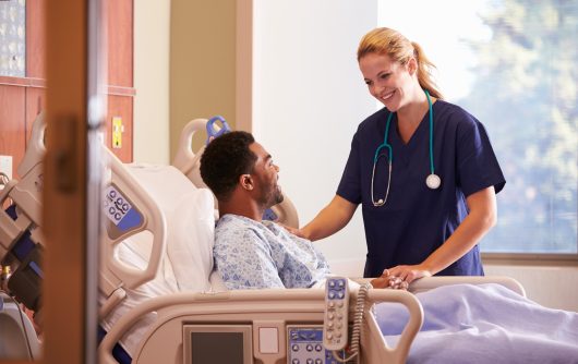 Female Doctor Talking To Male Patient In Hospital Bed