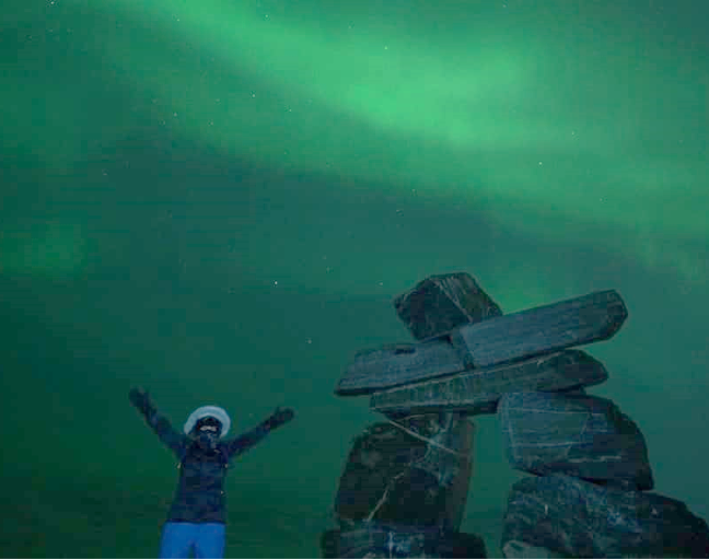 Kathleen Lambert St. Hilaire under northern lights beside inukshuk