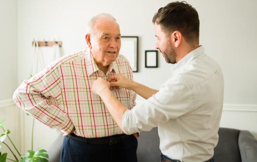 Caring young son helping his old happy elderly father to change clothes before going out of the house together