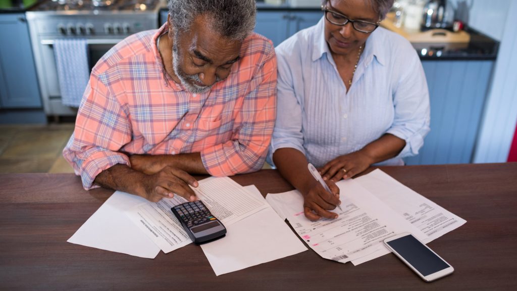 A senior couple filling out some forms. The man is using a calculator.