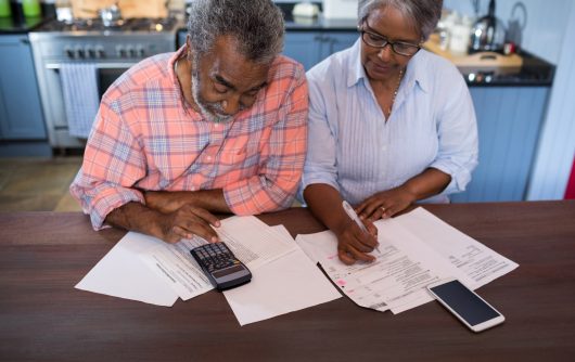 A senior couple filling out some forms. The man is using a calculator.