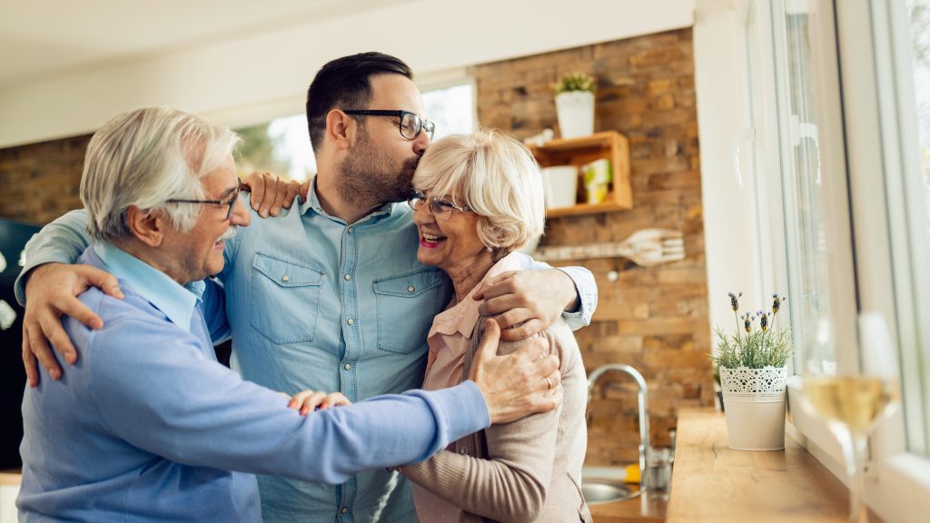 Affectionate man embracing his senior parents while greeting them in the kitchen.