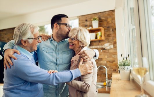 Affectionate man embracing his senior parents while greeting them in the kitchen.