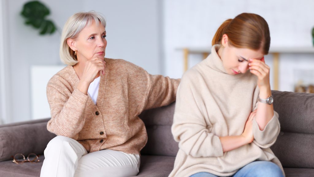 Two upset women sitting on the sofa. One of them looks disappointed.