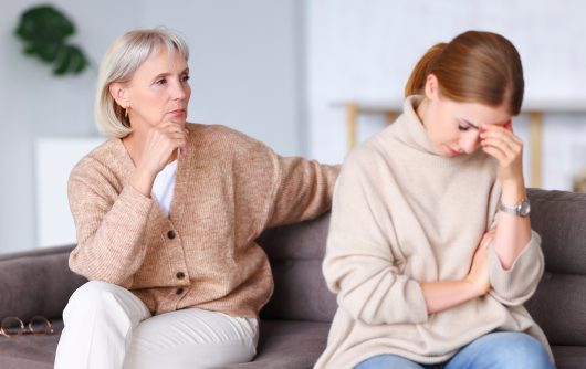 Two upset women sitting on the sofa. One of them looks disappointed.