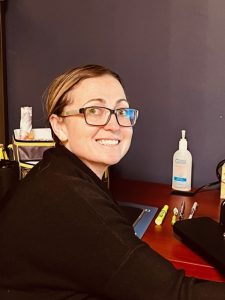 women with glasses smiling at camera at her desk