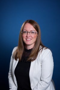 Woman with brown hair, glasses, smiling at camera.