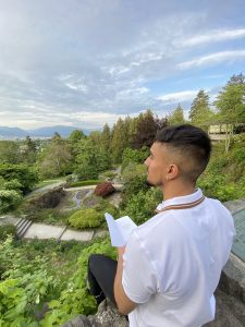 Man sitting outside, book in hand, looking out towards nature.