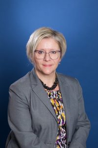 Blonde woman with glasses smiling in front of blue background