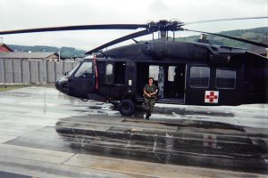 A woman in military uniform sitting at the doors of a grounded helicopter