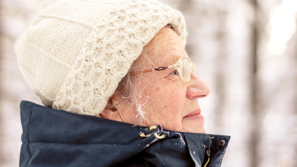 Portrait of a senior elderly woman walking in a snowy forest.A woman with glasses enjoys a sunny day.Active rest outdoors of mature people.Healthy lifestyle concept.