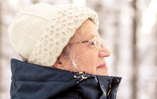 Portrait of a senior elderly woman walking in a snowy forest.A woman with glasses enjoys a sunny day.Active rest outdoors of mature people.Healthy lifestyle concept.