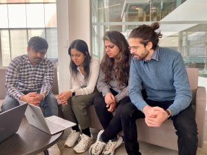 A group of four students looking over a laptop