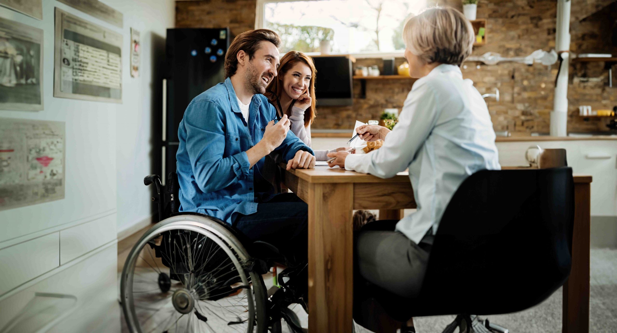 Caregiver, a man in a wheelchair, and a woman sitting and talking at a table
