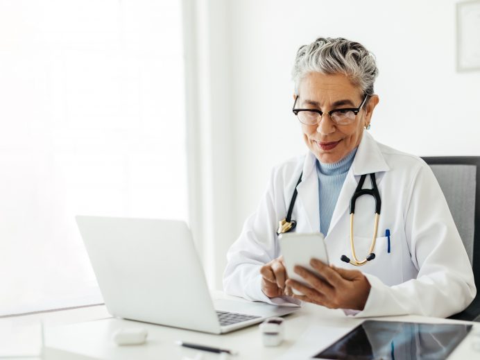 Tech-savvy senior doctor using a smartphone in her office