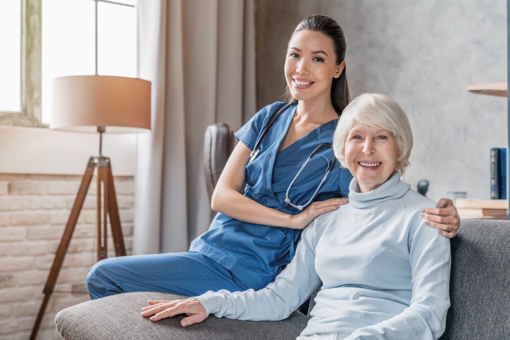 healthcare worker and elderly woman sitting on a grey couch
