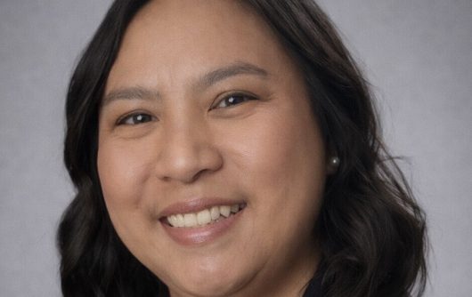 Portrait d'une femme souriante aux cheveux bruns ondulés mi-longs.
