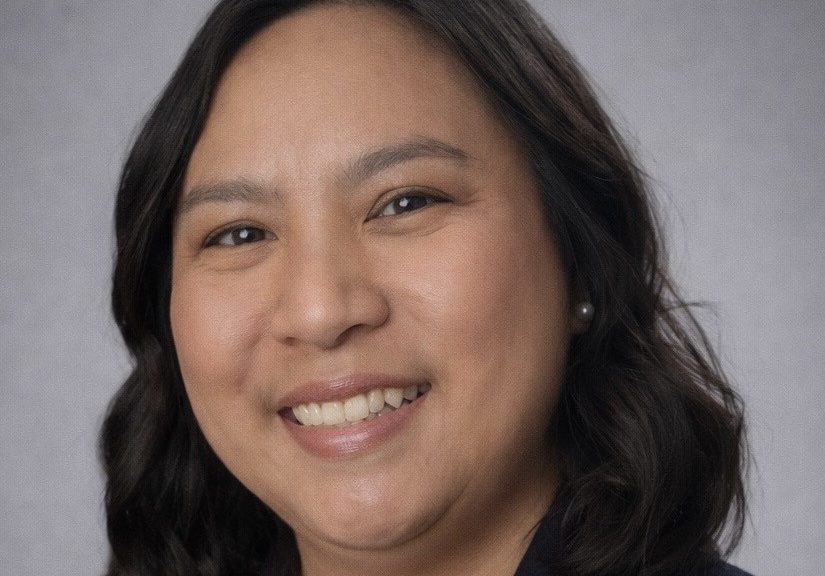 A studio portrait of a smiling woman with shoulder-length, dark wavy hair.