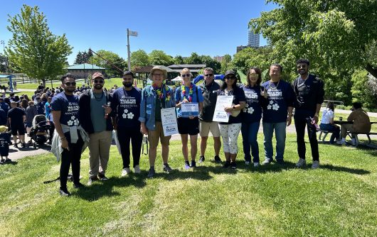 A group of ten people stands in a line on a grassy hill on a sunny day, posing for a photo at an IG Wealth Management Walk for Alzheimer's event.