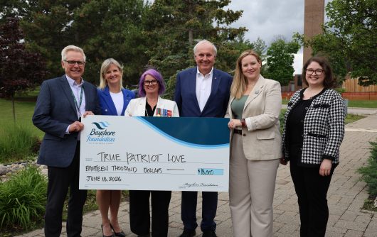 Six people standing outdoors holding a large ceremonial check from the Bayshore Foundation for $18,000, made out to True Patriot Love and dated June 18, 2026.